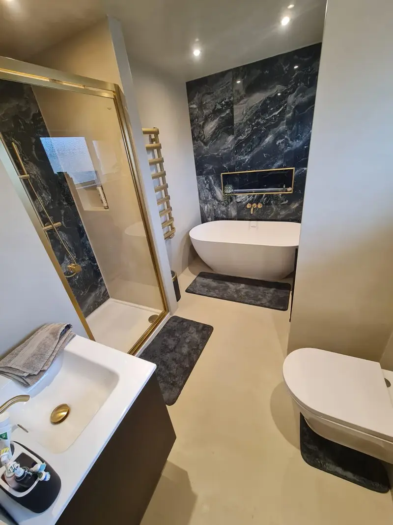 Bathroom with seamless cream microcement floor and walls, freestanding bath and dark marble feature wall