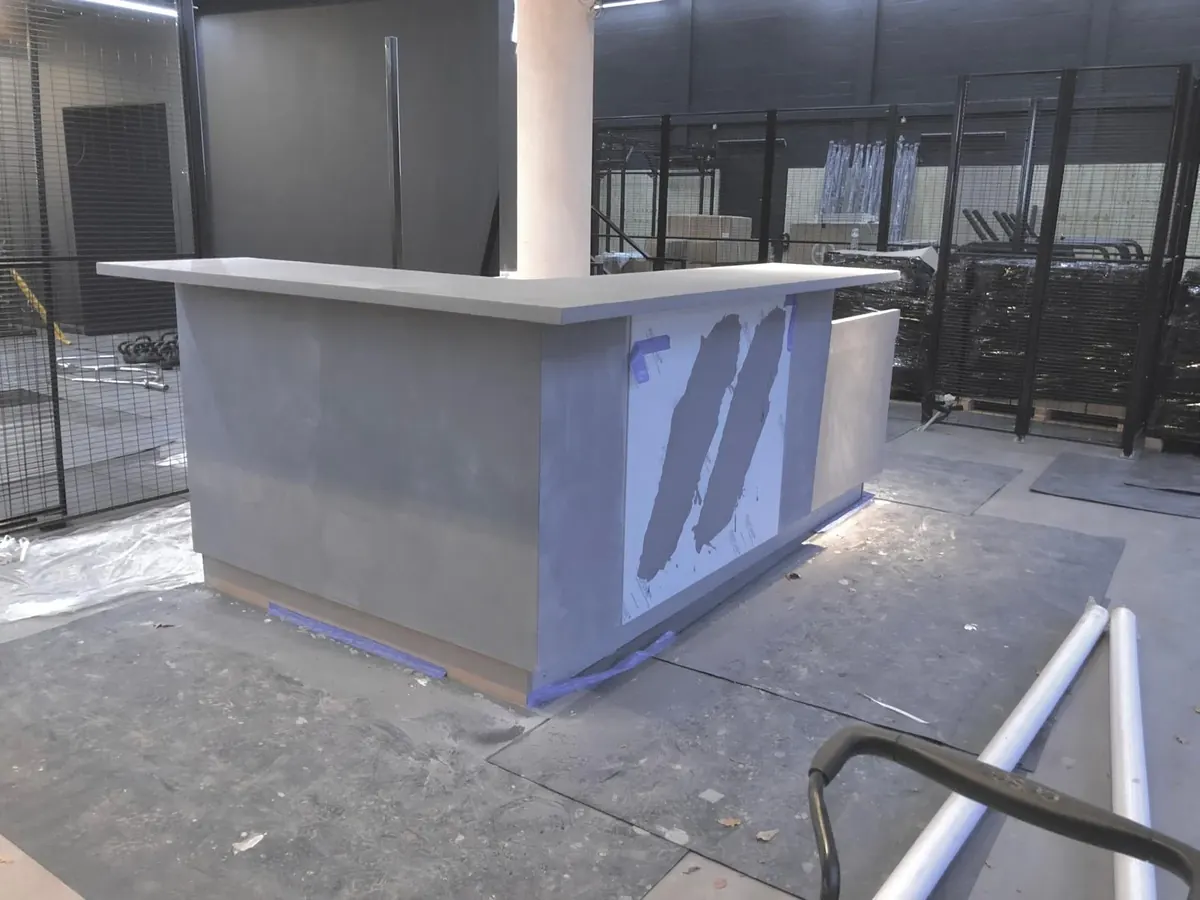 L-shaped commercial reception counter coated in grey microcement, with the logo panel still under protective film